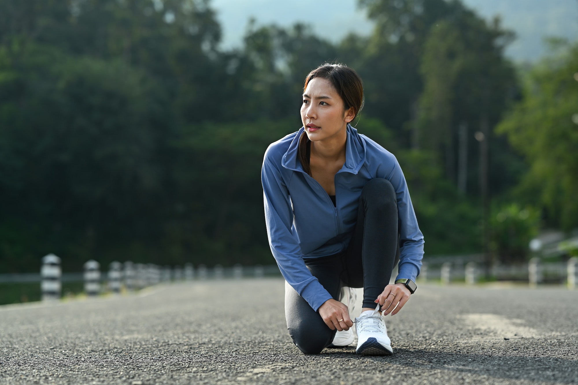 Image of asian woman tying shoelace before running outdoors.